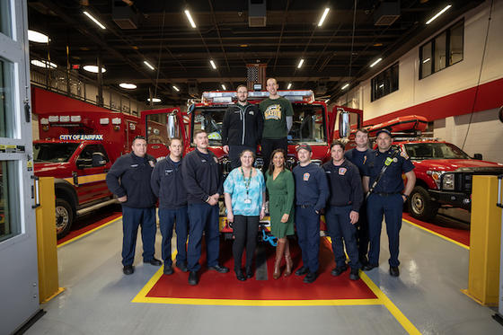 Marcus Brick (top left), Mark Radish (top right), Allison McKay (bottom center left), Allison Miner (bottom center right), and the firefighters from Station 33 pose in front of firetrucks. Photo by Evan Cantwell/Creative Services.