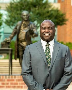 University President Gregory Washington wearing a suit and standing in front of the Mason Statue