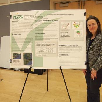 Mason student in professional attire standing next to a research poster.