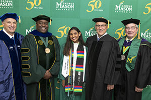 Provost Mark Ginsberg (left to right), President Gregory Washington, student commencement speaker Bhagya Nair, commencement keynote speaker Stu Shea, and Rector Jimmy Hazel pose for a group photo in the hospitality room during the 2022 Spring Commencement Ceremony at EagleBank Arena. Photo by Evan Cantwell/Creative Services/George Mason University