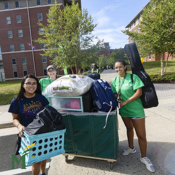 Three students roll a bin full of student belongings at Freshman Move-in at George Mason University. 