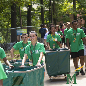 Members of Move Crew at George Mason University roll green bins outside at George Mason University to help new students move their luggage boxes. The students who are part of Move Crew are all wearing green "Move Crew" T-Shirts.
