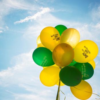 A bunch of green and gold balloons are floating against a bright blue sky.