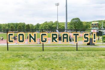 A chain link fence along a Mason athletic field is decorated with green and gold letters that read "Congrats!"