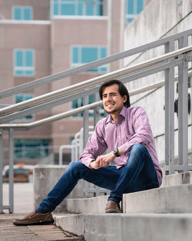 Arturo Barrera sitting on stairs outside at the Mason Square campus.