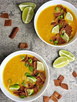 Two bowls of lentil soup are garnished with lime. Extra lime wedges are nearby on the table.