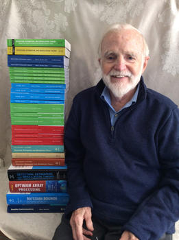 Harry Van Trees, professor emeritus at Mason CEC, wears a dark-blue sweater and smiles next to a stack of IT books