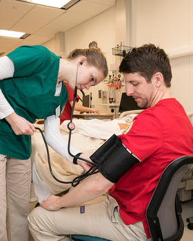 A student practices taking blood pressure on a volunteer.