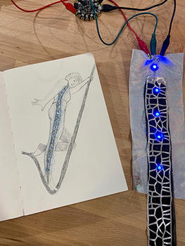 A sketch of a performer on paper and a piece of an LED prototype that will be embedded in an aerial performer's costume.