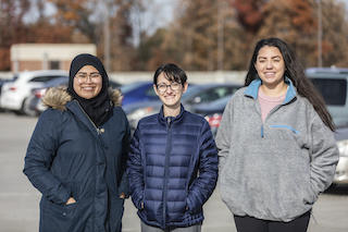 Nada Adibah, Jenna Krall, and Gabriella Cuevas stand next to each other in a parking lot and smile for the camera.